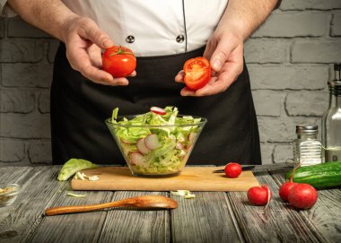 A professional chef skillfully holds a halved tomato while preparing a fresh salad with lettuce and radishes. The vibrant ingredients create an inviting atmosphere in the kitchen.