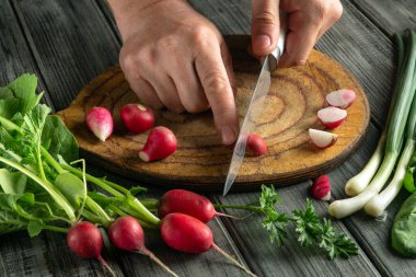 Hands skillfully chop radishes and prepare green onions on a cutting board surrounded by fresh herbs. A vibrant kitchen setting enhances the cooking process.