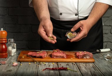 In a rustic kitchen, a chef is seen seasoning beef steaks with a mix of spices and herbs. The atmosphere is cozy with wooden details and fresh ingredients on the table.