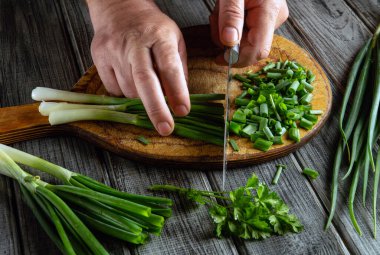Hands skillfully chop green onions and cilantro on a wooden board, preparing ingredients for a flavorful dish in a home kitchen. Fresh herbs enhance the meal.