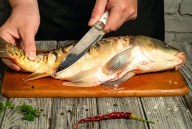 Bir aşçı ustaca fileto yapar büyük bir balığı ahşap bir tahtada, sıcacık bir mutfakta. Hazırlık alanını çevreleyen taze otlar ve baharatlar aşçılık sanatını ön plana çıkarıyor..