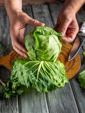 Taze lahana tahta kesme tahtasının üzerinde hazırlanıyor. Eller tabakaları dikkatlice soyarken, yakınlarda bir bıçak ve otlar yemek pişirmeye hazır olduklarını gösteriyor..