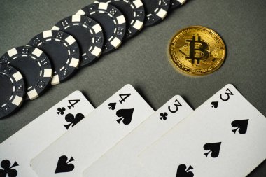 Poker fişleri, üçlü ve dörtlü çiftleri gösteren kart oyunlarının yanında düzgünce düzenlenir. Yüzeyde parlak bir Bitcoin, geleneksel ve dijital oyun karışımı bir şey yaratıyor..