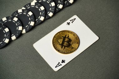Siyah ve beyaz poker fişleri ile çevrili, gri bir yüzeye karşı, bir sinek as üzerine parlak bitcoin yerleştirilir. Bu düzen kripto para ve kumarın karışımını temsil ediyor..