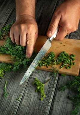 Ahşap kesme tahtasındaki yeşil otları ustalıkla kesen eller, iş başında bir bıçak sergiliyor. Taze dereotu ve doğranmış sebzeler canlı bir yemek sahnesi yaratır..