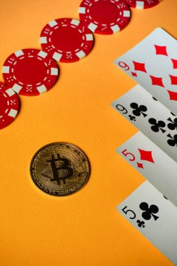 Bir Bitcoin, turuncu bir masanın üzerinde kırmızı poker fişleri ve iki çift elin yanında yer alır. Heyecan havayı dolduruyor..
