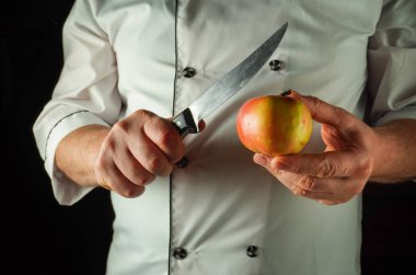 Yetenekli bir şef bir elinde parlak bir bıçak, diğer elinde taze bir elma tutar. Sahne, dilimleme, altı çizilmeden önceki anı yakalar..