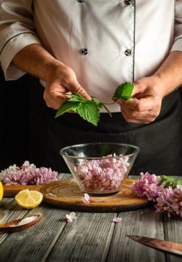 Bir şef zarif bir şekilde taze nane yaprakları hazırlar. Etrafı çiçek açan leylak çiçekleri ve limon dilimleriyle çevriliyken mutfak ortamında mutfak yaratıcılığını gösterir..