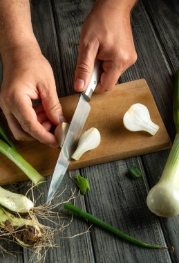 Tahta kesme tahtasındaki taze soğanları ustalıkla dilimle dilimle. Canlı sebzeler kırsal gri masa ile tezat oluşturarak canlı bir mutfak sahnesi oluşturuyor..