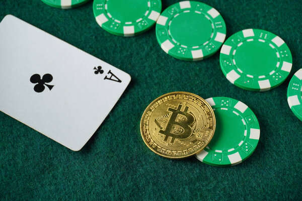 A digital currency, bitcoin, sits on a green poker table alongside casino chips and an Ace of clubs card. The setting captures a vibrant gambling atmosphere, combining traditional and modern gaming.