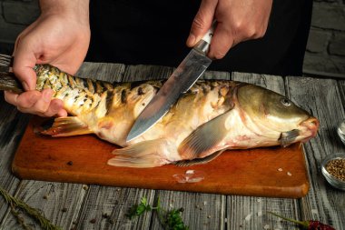 Bir insan, parlak bir mutfakta ahşap bir kesme tahtasında ustalıkla taze bir balığı temizler ve fileto yapar. Taze otlar ve baharatlar yakınlarda, mutfak sahnesini güzelleştiriyor..