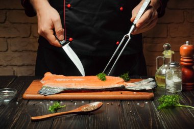 Yetenekli bir şef taze somon filetosu hazırlamak için bıçak ve mutfak ortamında baharat ve şifalı otlar kullanır..