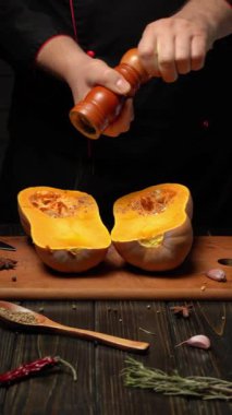 Parlak turuncu tereyağı kabağı ikiye bölünür ve tohumları ortaya çıkar. Bir şef, sıcak bir mutfakta ahşap kesme tahtası üzerinde çalışırken tadını arttırmak için biber ekliyor..