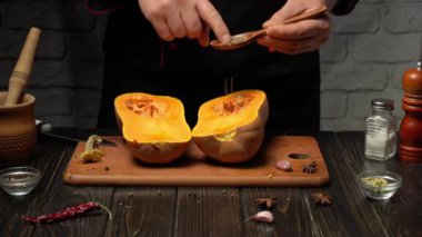 Bir şef ustalıkla olgun bir kabağı yarıya indirir ve küçük bir kaşık kullanarak baharat ekler. Sıcak, kırsal mutfak yemek malzemeleri ve aletlerle dolu, davetkar bir atmosfer yaratıyor..