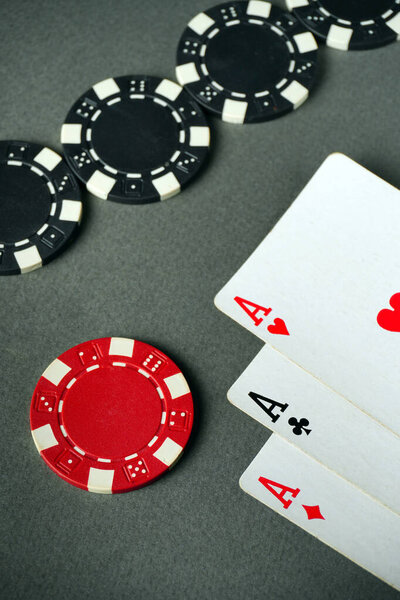Players are engaged in a game of poker, showcasing three aces and various chips on a gray table. The scene captures the excitement and strategy involved in card games.