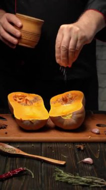 Bir şef ahşap bir tahtaya yerleştirilmiş taze tereyağlı balkabağı yarımlarına nazikçe tuz serpiyor. Mutfak rahat ve davetkar, doğal ışıkla dolu..