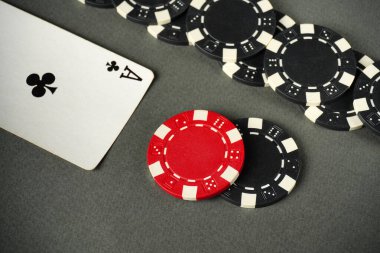 Kırmızı poker fişi ve siyah çipler, gri bir masa yüzeyindeki sinek ası, heyecan verici bir kart oyununa işaret ediyor. Oyuncular odaklanmış, eğleniyorlar..
