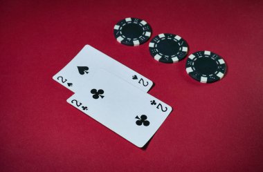 İki iskambil kağıdı, iki maça ve iki sinek, kırmızı bir masanın üzerine birkaç siyah poker çipinin yanına konur, bu da oyun gecesi atmosferinin rekabetçi olduğunu gösterir..