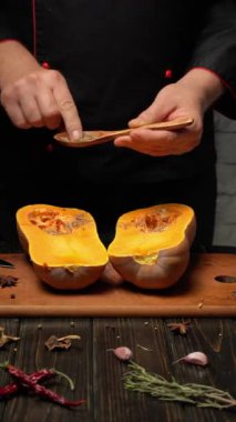 Bir şef taze kabağı dikkatlice hazırlar, onu ikiye ayırır ve ahşap kaşıkla baharat ekler. Sıcak mutfak ortamı sıcak yemek pişirme atmosferini geliştirir..