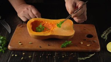 Taze tereyağlı kabağı ustalıkla temizlerken lezzeti arttırmak için otlar ekliyor. Hazırlık, yakındaki mutfak eşyalarıyla birlikte kırsal ahşap bir kesme tahtasının üzerinde gerçekleşiyor..