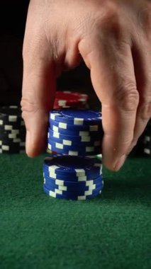 Bir el, canlı bir kumarhanede yeşil keçeli kalemle kaplı bir masaya ustalıkla mavi poker fişleri yığar. Oyuncular arka plandaki kart oyununa odaklanmış durumdalar
