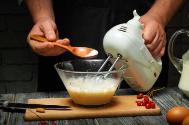 Samimi bir mutfakta, bir insan temiz bir kaseye malzemeleri karıştırıcı kullanarak karıştırır. Şeker ahşap bir kaşıkla eklenirken taze yumurta ve badem yakınlarda..