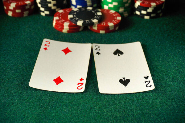 Two cards showing the 2 of diamonds and 2 of spades are placed on a green felt poker table. In the background, various colorful poker chips are stacked high, creating an exciting casino atmosphere.