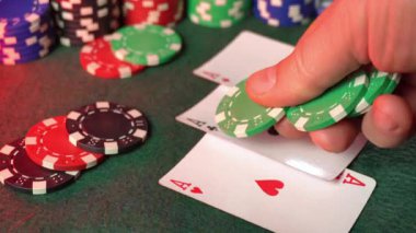 Bir kumarhane masasında iki as kazanan bir el tutarken bir oyuncu yeşil poker fişlerini kavrıyor. Yakınlarda renkli çipler yığılıyor, heyecan verici bir atmosfer yaratıyor..