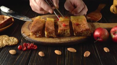 Elma, badem ve koyu ahşap bir yüzey üzerinde pişmiş ürünlerle çevrili parlak kirazlarla kaplı altın bir hamur işi. Bu sahne rahat bir mutfak atmosferini yakalar..