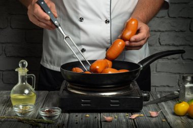 Beyaz üniformalı bir şef bir restoranın mutfağında baharat ve kahvaltı malzemeleriyle sosis hazırlar..