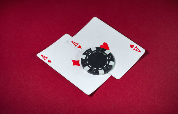 Two ace playing cards lie on a smooth red surface with a black and white poker chip placed on top. This scene captures the excitement of a casino game, showcasing high stakes.