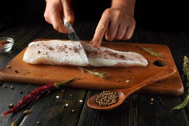 Tahta kesme tahtasına yerleştirilmiş taze balık filetosu kesilir. Çeşitli baharatlar ve otlar balığı çevrelemiş, bir mutfakta renkli ve lezzetli bir sahne yaratmış..