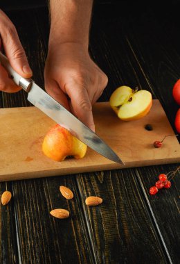 Tahta bir kesme tahtasıyla parlak bir elmayı ikiye böler. Badem ve kırmızı böğürtlenler etrafa saçılmış güneşli bir öğleden sonra boyunca canlı bir mutfak sahnesi yaratıyorlar..
