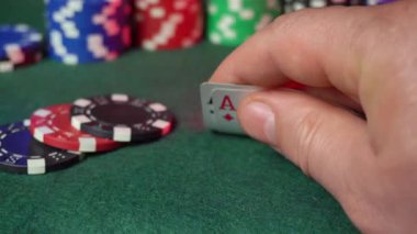 Yeşil bir keçeli masada poker oynarken bir el as kartı tutar. Renkli çipler, oyunun heyecanını yakalayan rekabetçi bir atmosferi gösteriyor.