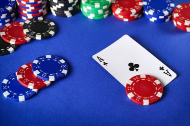 Kırmızı, siyah ve mavi poker fişleri yayılmış mavi bir masada. Bir kart oyunu için çiplerin yanına bir sinek ası yerleştirilir.