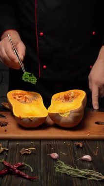 Bir şef ahşap bir tahtanın üzerinde bir tereyağlı kabağı ikiye böler. Kabağın parlak turuncu eti görünür. Şef üzerine maydanoz filizini yerleştirirken diğer malzemeler etraflarını sarıyor..