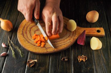 Eller, diğer taze sebzelerle çevrili, kırsal kesme tahtasındaki canlı havuçları doğruyor, mutfakta sıcak ve davetkar bir atmosfer yaratıyor..