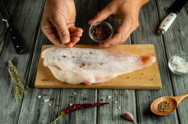 Bir şef, yaşlı bir balık leşini elleriyle mevsimlendirir. Baharat ve tuz aroma ve aroma için mutfak tezgahına saçılmıştır..