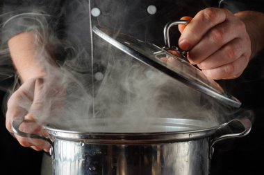 Yoğun bir restoran mutfağında buhar yükselirken bir şef tencerenin kapağını açıyor. Sahne akşam yemeği hazırlıklarını gösteriyor. Odaklanmış aşçılık görevleri yapılıyor..