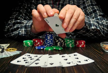 Bir masada otururken elinde sinek ası tutan bir kişi var. Etraflarında bir sürü poker fişi var ve masaya da bir kaç oyun fişi serilmiş..