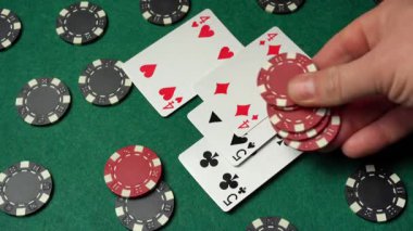 Yeşil keçeli masa üzerinde poker oynarken bir oyuncu iki çift iskambil kağıdına kırmızı çip yerleştirir. Başarılı bir galibiyet için bahis oynanıyor..