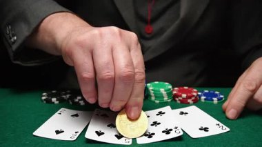 Bir adam masaya Bitcoin para koyarken bir dizi oyun kartına odaklanır. Yakınlarda renkli poker fişleri var. Akşamları kumarhane gibi..