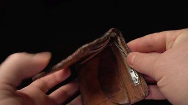 Eller nazikçe bir fermuarlı deri cüzdanı açar ve içindeki katlanmış parayı ortaya çıkarır. Cüzdanın dokusuna ve içindeki paranın görünür detaylarına odaklanıyoruz.