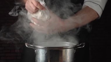 Şefin elleri hamur köftesiyle dolu bir torbayı kaldırır, onları kızgın bir tencereye döker, profesyonel bir mutfakta koyu tuğladan bir arka plan oluşturur.