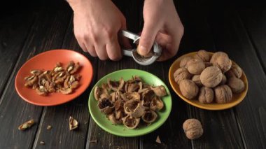 Fındık kırmak için fındık kıran eller, içindeki cevizi ortaya çıkarıyor, içi boş ceviz kabukları ve kabuklu fındıklar, iyi aydınlatılmış bir mutfak ortamında renkli tabaklara yerleştirilmiş.