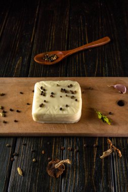 Peynir, karabiber, sarımsak ve otlarla çevrili ahşap bir tahtanın üzerinde oturur. Yakınlarda daha fazla biberli bir tahta kaşık var. Bu yemek hazırlıklarını gösteriyor..