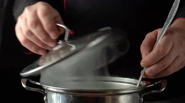 Şef eller sıcak bir tencerenin kapağını kaldırır, ve diğer yandan bir kepçe karabuğday, mutfak gereçleri ve malzemelerle pişirme sürecini gösterir..