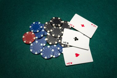 Bir grup poker fişi ve iskambil kağıdı yeşil bir masanın üzerinde. Ayarda çeşitli renkli çipler ve üç oyun kartı gösteriliyor. Oyuncular büyük ihtimalle bir oyunla meşgul..