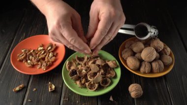 Açık ceviz kırmakla meşgul bir insanın elleri, kabukları fındıklardan dikkatlice ayırıyor, mutfak ortamında ahşap bir masa üzerine renkli tabaklar yerleştirilmiş.