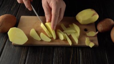 Elleri ustalıkla taze patatesleri ince şeritlere ayırıyor ahşap bir kesim tahtasının üzerinde, bütün patatesler kırsal ahşap bir masa yüzeyinde kesme tahtasının etrafına yerleştiriliyor.